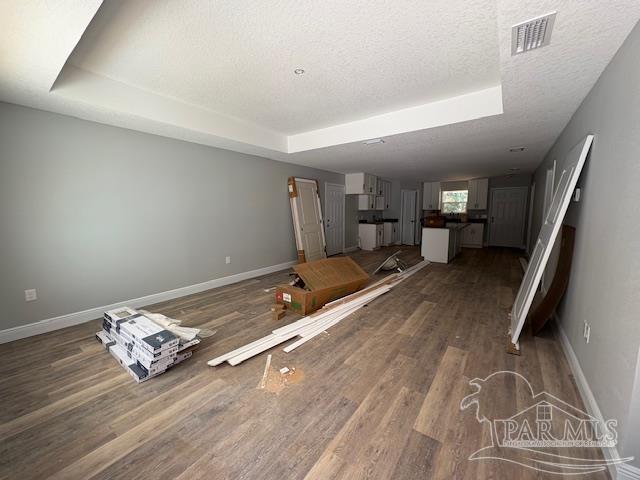 unfurnished living room featuring a textured ceiling, wood finished floors, visible vents, baseboards, and a raised ceiling