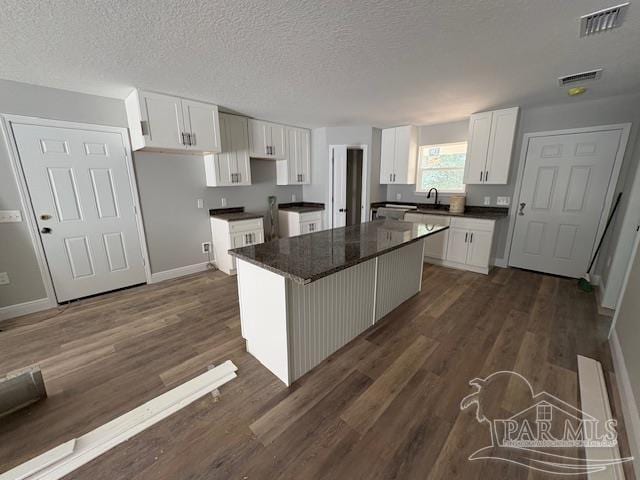 kitchen with dark wood-style flooring, dark countertops, visible vents, white cabinets, and a sink