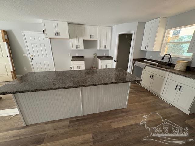 kitchen featuring a sink, white cabinets, dark wood-style flooring, and a center island