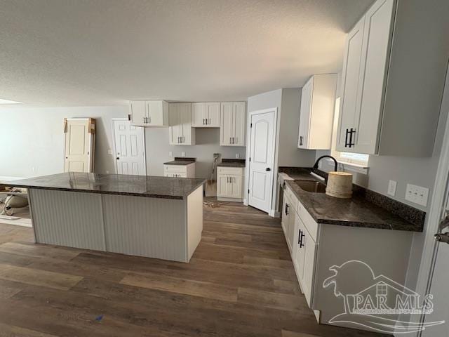 kitchen featuring dark wood finished floors, dark countertops, a kitchen island, white cabinetry, and a sink