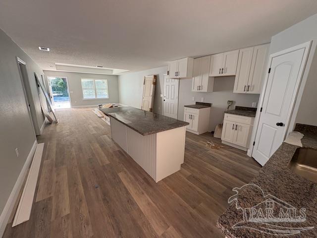 kitchen featuring a center island, dark countertops, dark wood-type flooring, open floor plan, and white cabinets