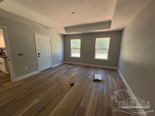 interior space featuring baseboards, a textured ceiling, a tray ceiling, and dark wood-style flooring