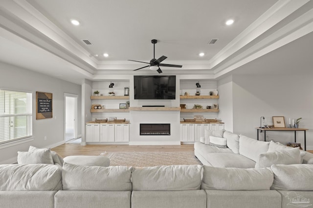 5534 Blake Ln, Pace, FL 32571 - living area featuring a raised ceiling, light wood-type flooring, a ceiling fan, a glass covered fireplace, and crown molding