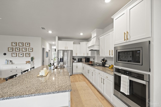 5534 Blake Ln, Pace, FL 32571 - kitchen with stainless steel appliances, an island with sink, white cabinets, light wood-type flooring, and recessed lighting