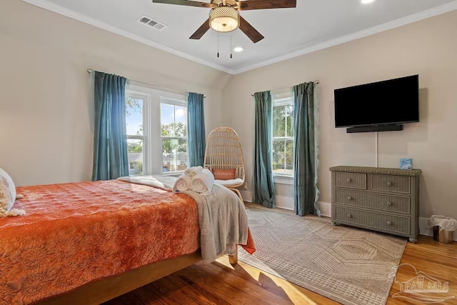 bedroom with wood finished floors, visible vents, crown molding, and multiple windows