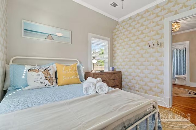 bedroom featuring wood finished floors, crown molding, visible vents, and baseboards
