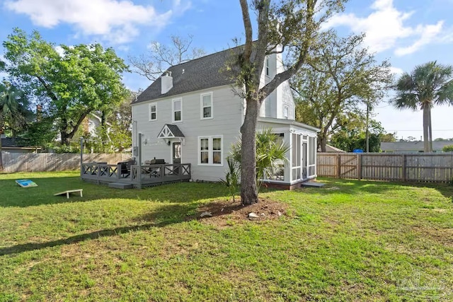 rear view of house featuring a lawn, a wooden deck, a sunroom, and a fenced backyard