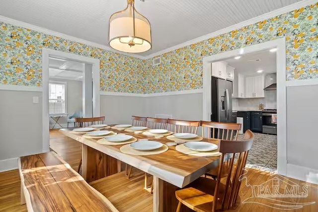 dining area with crown molding, a wainscoted wall, wallpapered walls, and light wood-style flooring