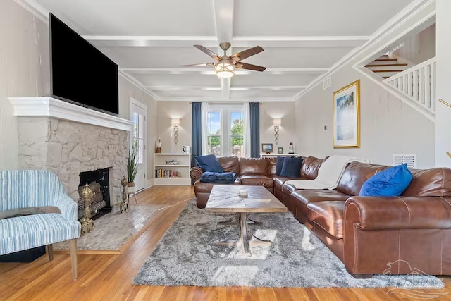 living area featuring stairway, ceiling fan, coffered ceiling, a stone fireplace, and wood finished floors