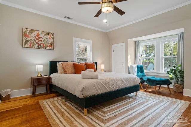 bedroom with a ceiling fan, visible vents, baseboards, ornamental molding, and wood finished floors