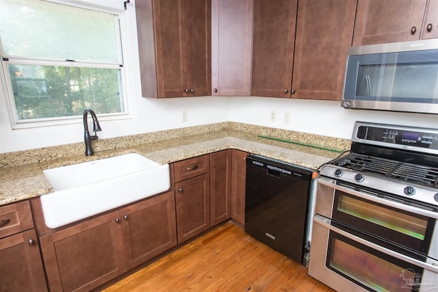 kitchen with a sink, stainless steel appliances, light stone countertops, and light wood finished floors