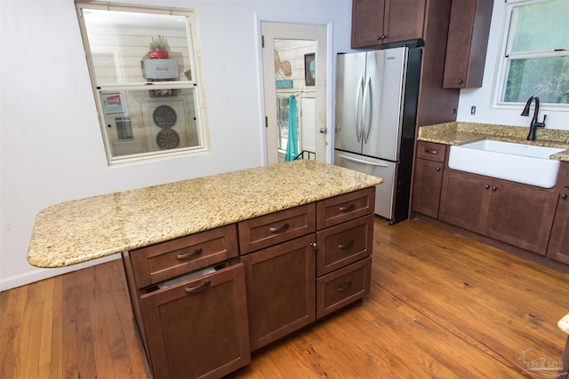 kitchen featuring a sink, light stone counters, wood finished floors, and freestanding refrigerator