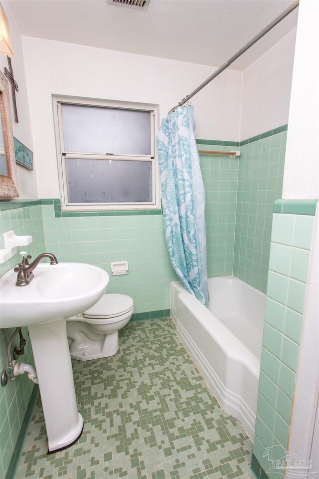 full bathroom with visible vents, toilet, tile walls, and shower / tub combo with curtain