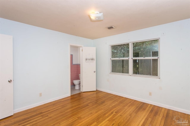 empty room with hardwood / wood-style flooring, baseboards, and visible vents