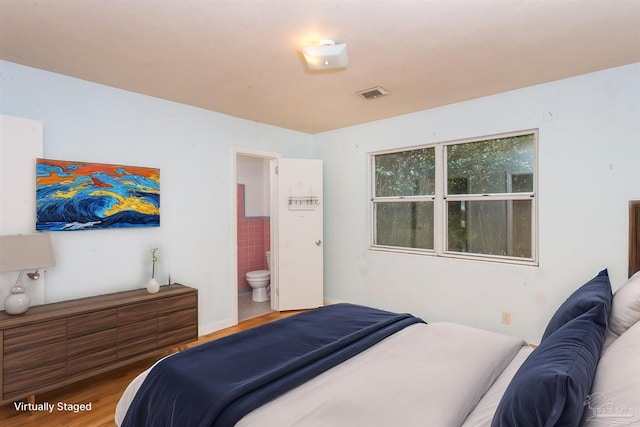 bedroom with wood finished floors, visible vents, and connected bathroom