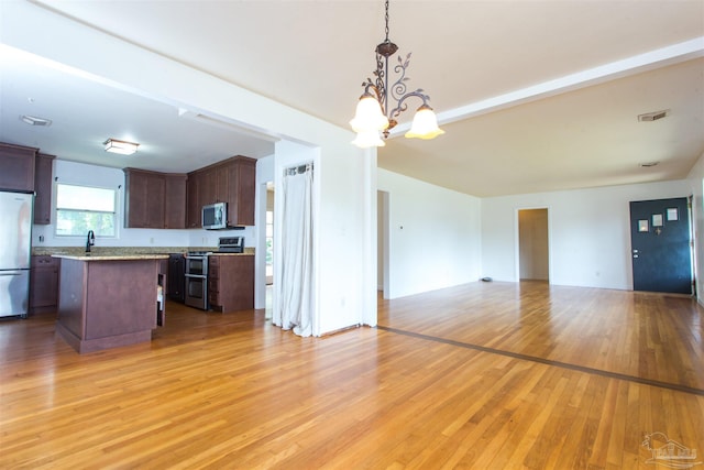 kitchen with decorative light fixtures, a kitchen island, open floor plan, appliances with stainless steel finishes, and light wood finished floors