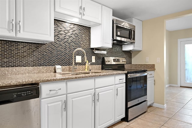 kitchen with stainless steel appliances, light tile patterned floors, a sink, tasteful backsplash, and white cabinetry