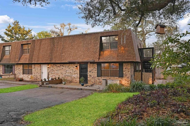 view of front of house featuring brick siding, roof with shingles, and mansard roof