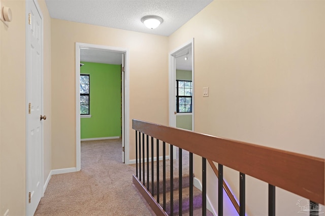hall featuring a textured ceiling, baseboards, light carpet, and an upstairs landing