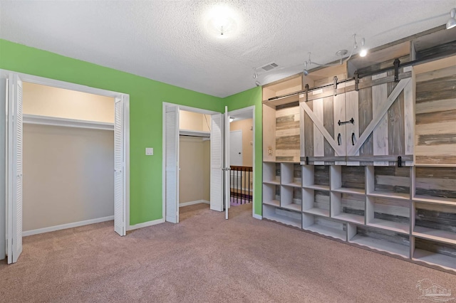 unfurnished bedroom featuring a barn door, a textured ceiling, two closets, carpet, and visible vents