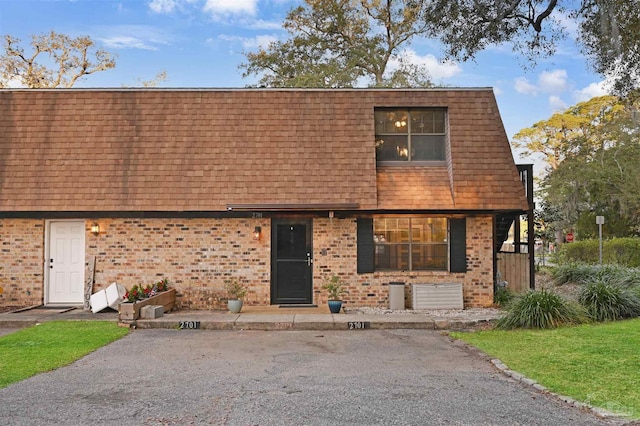 view of front of house with brick siding, roof with shingles, and mansard roof