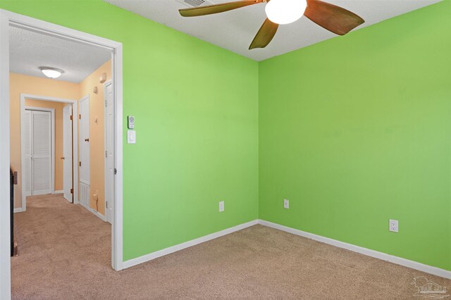 carpeted spare room featuring a textured ceiling, a ceiling fan, and baseboards