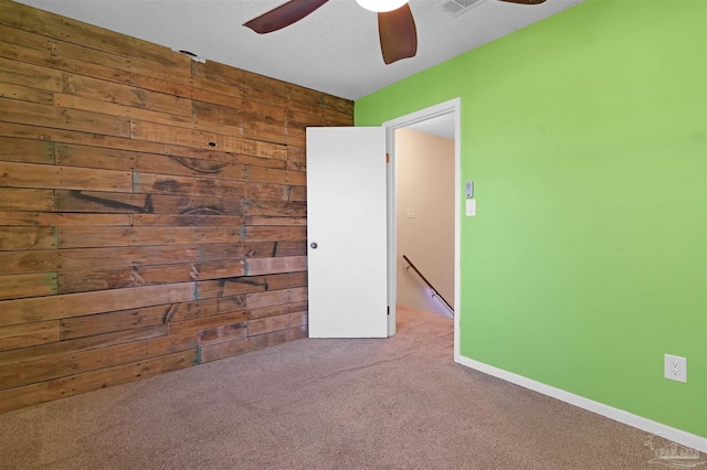 carpeted spare room featuring wood walls, baseboards, and a ceiling fan