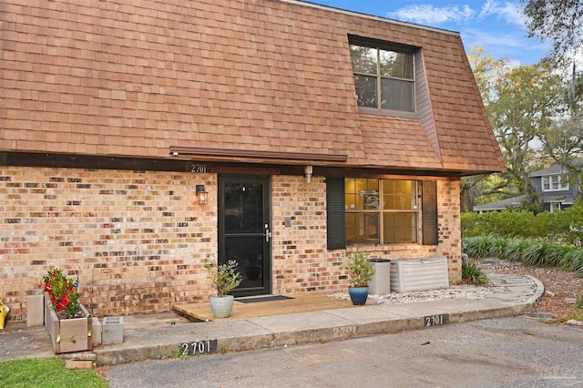 townhome / multi-family property featuring brick siding, roof with shingles, and mansard roof