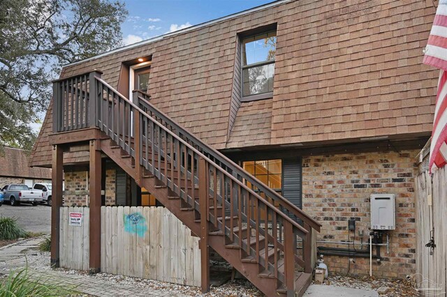 back of property with brick siding, roof with shingles, stairs, and mansard roof