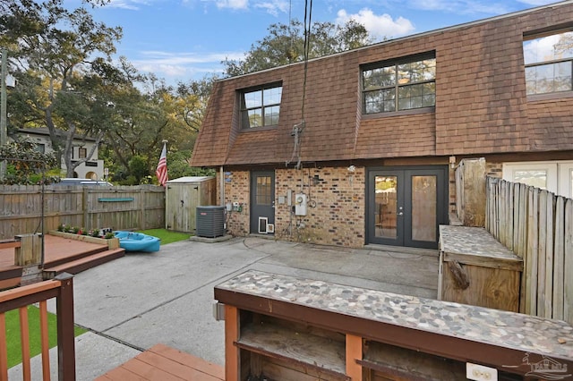 back of property with fence, mansard roof, a patio area, french doors, and brick siding