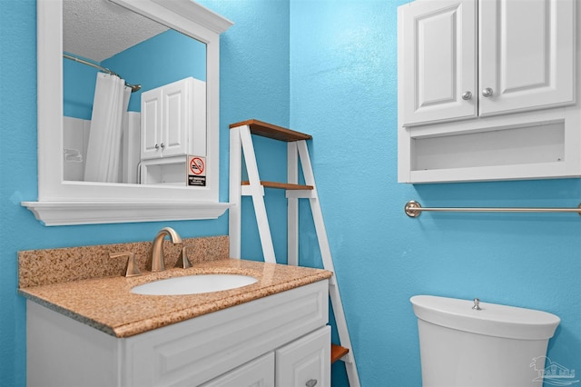 full bath featuring toilet, a textured wall, and vanity