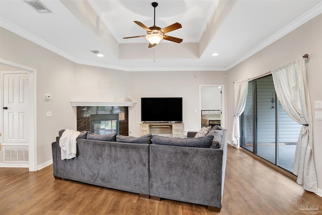 living room featuring a tiled fireplace, a raised ceiling, wood-type flooring, and ornamental molding