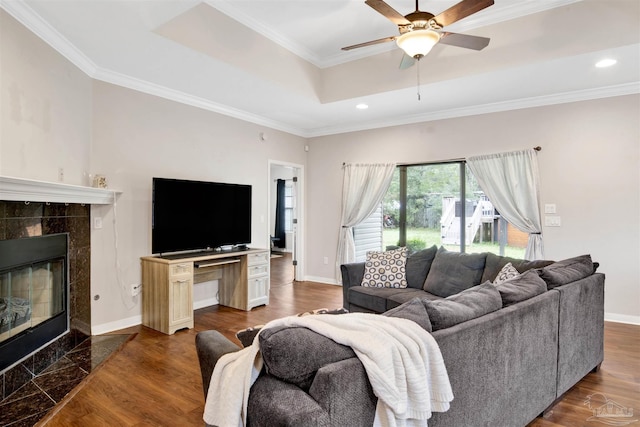 living room with ceiling fan, a tray ceiling, a fireplace, ornamental molding, and dark hardwood / wood-style flooring