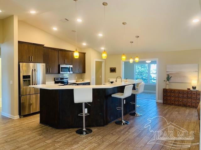 kitchen with a large island with sink, appliances with stainless steel finishes, a kitchen bar, hanging light fixtures, and vaulted ceiling