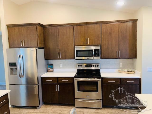 kitchen featuring tasteful backsplash, appliances with stainless steel finishes, vaulted ceiling, and dark brown cabinetry