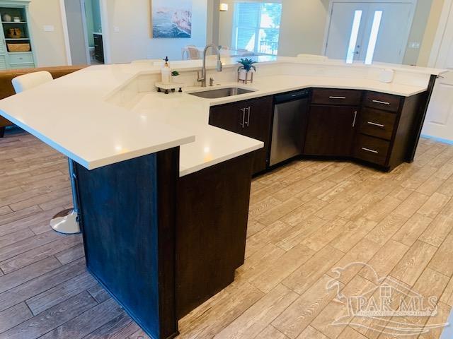 kitchen featuring a kitchen island with sink, light wood-type flooring, stainless steel dishwasher, and sink