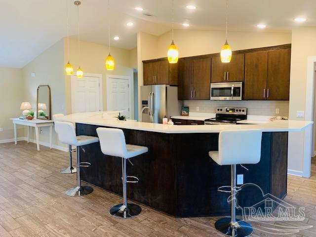 kitchen featuring stainless steel appliances, pendant lighting, a breakfast bar, and vaulted ceiling