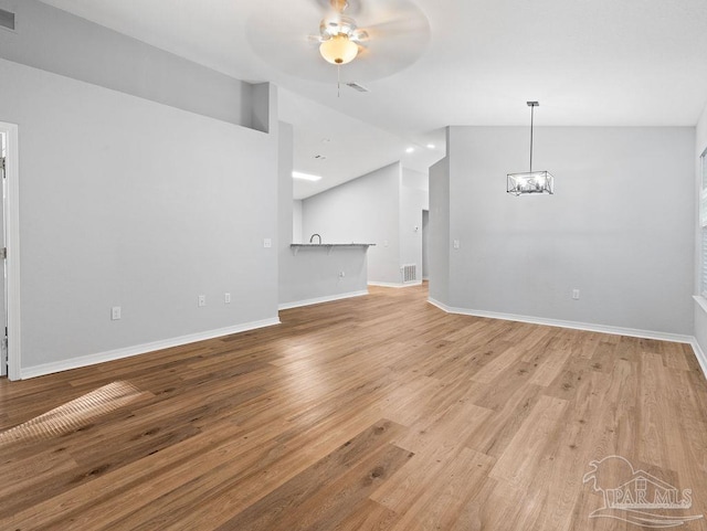 unfurnished living room featuring ceiling fan with notable chandelier, visible vents, baseboards, vaulted ceiling, and light wood-type flooring