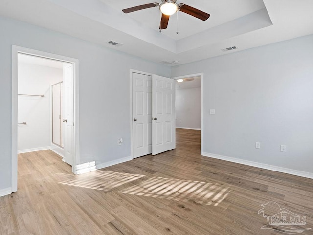 unfurnished bedroom with light wood-style flooring, visible vents, a raised ceiling, and baseboards