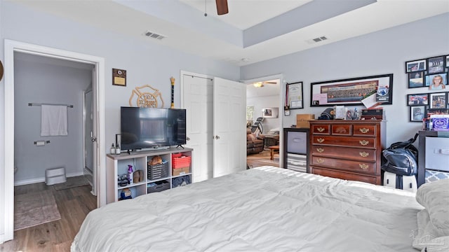 bedroom featuring baseboards, a tray ceiling, visible vents, and wood finished floors