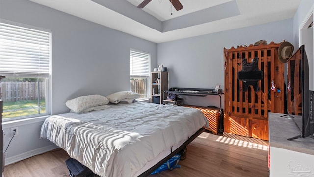 bedroom featuring ceiling fan, a tray ceiling, wood finished floors, and baseboards