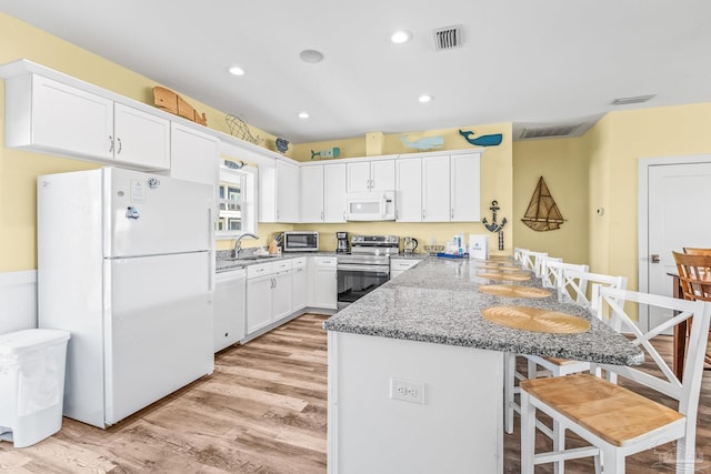 kitchen with white appliances, sink, light wood-type flooring, kitchen peninsula, and white cabinetry