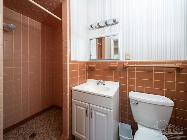 bathroom featuring vanity, toilet, tile walls, and a tile shower