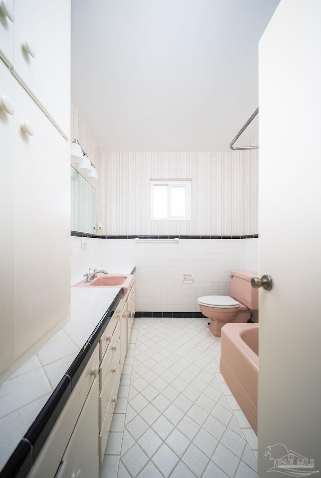 bathroom with tile walls, toilet, a bidet, vanity, and tile patterned floors