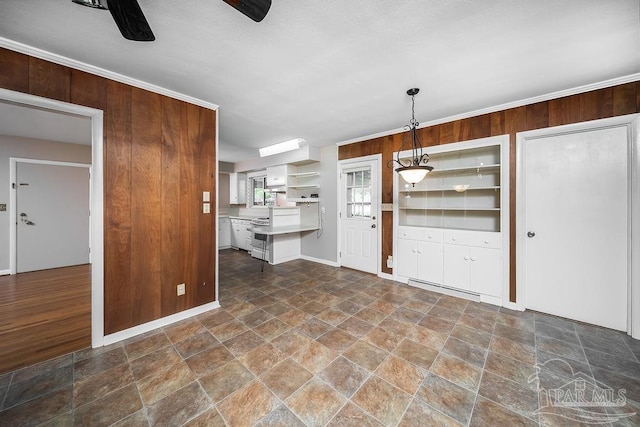 kitchen featuring ceiling fan, white cabinetry, ornamental molding, wood walls, and pendant lighting