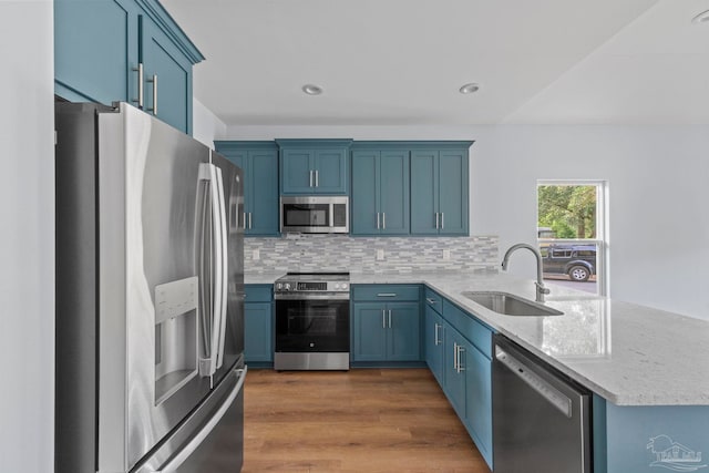 kitchen featuring sink, decorative backsplash, light stone countertops, appliances with stainless steel finishes, and kitchen peninsula