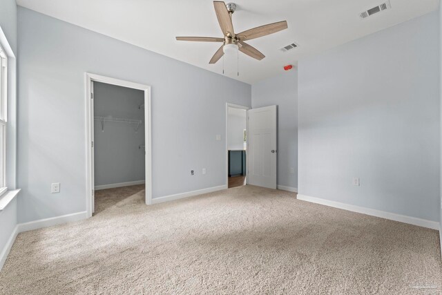 unfurnished bedroom featuring carpet flooring, a walk in closet, a closet, and ceiling fan