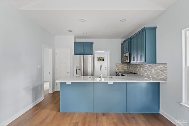 kitchen with kitchen peninsula, sink, blue cabinetry, appliances with stainless steel finishes, and wood-type flooring