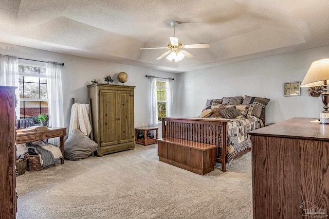 carpeted bedroom featuring ceiling fan, a textured ceiling, a tray ceiling, and multiple windows