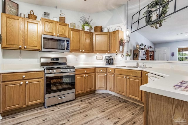 kitchen with kitchen peninsula, appliances with stainless steel finishes, vaulted ceiling, sink, and light hardwood / wood-style flooring